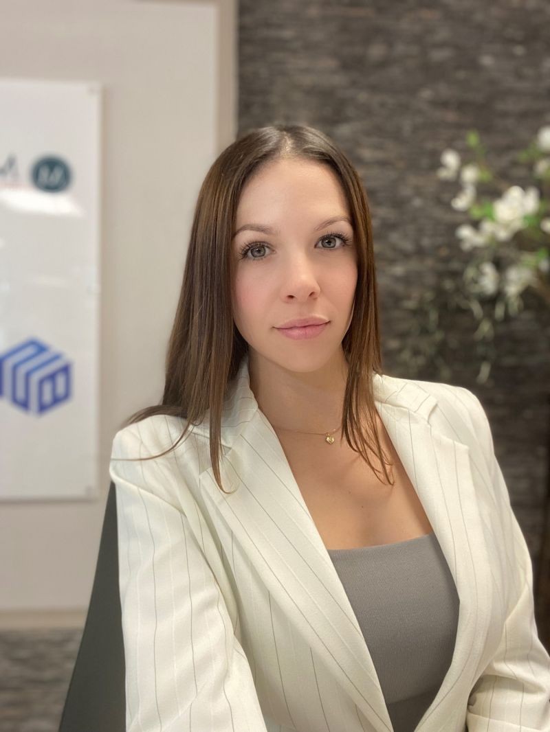 Woman in a white pinstripe blazer and gray top sitting indoors with a decorative background featuring flowers.